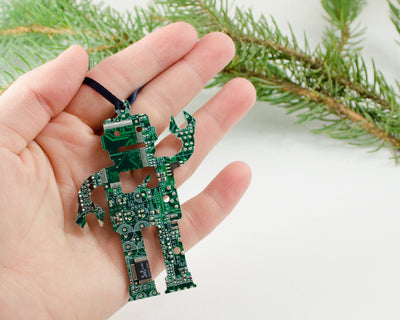 green circuit board ornament robot shape held in hand with evergreen