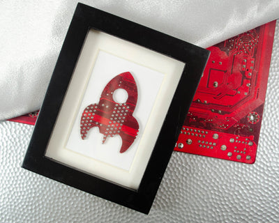 handmade framed artwork of a stylized rocket ship made from recycled red circuit board