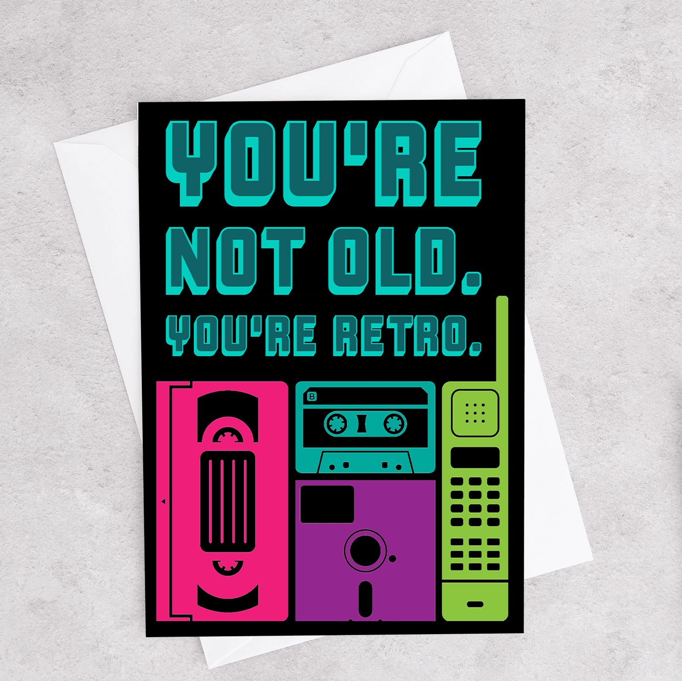 This birthday card says "You're Not Old. You're Retro." and shows a cassette tape, floppy disc, VHS, and old phone.